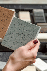 Image of woman's hand holding two pieces of granite to select.  One piece is an orangish brown, and the other gray.