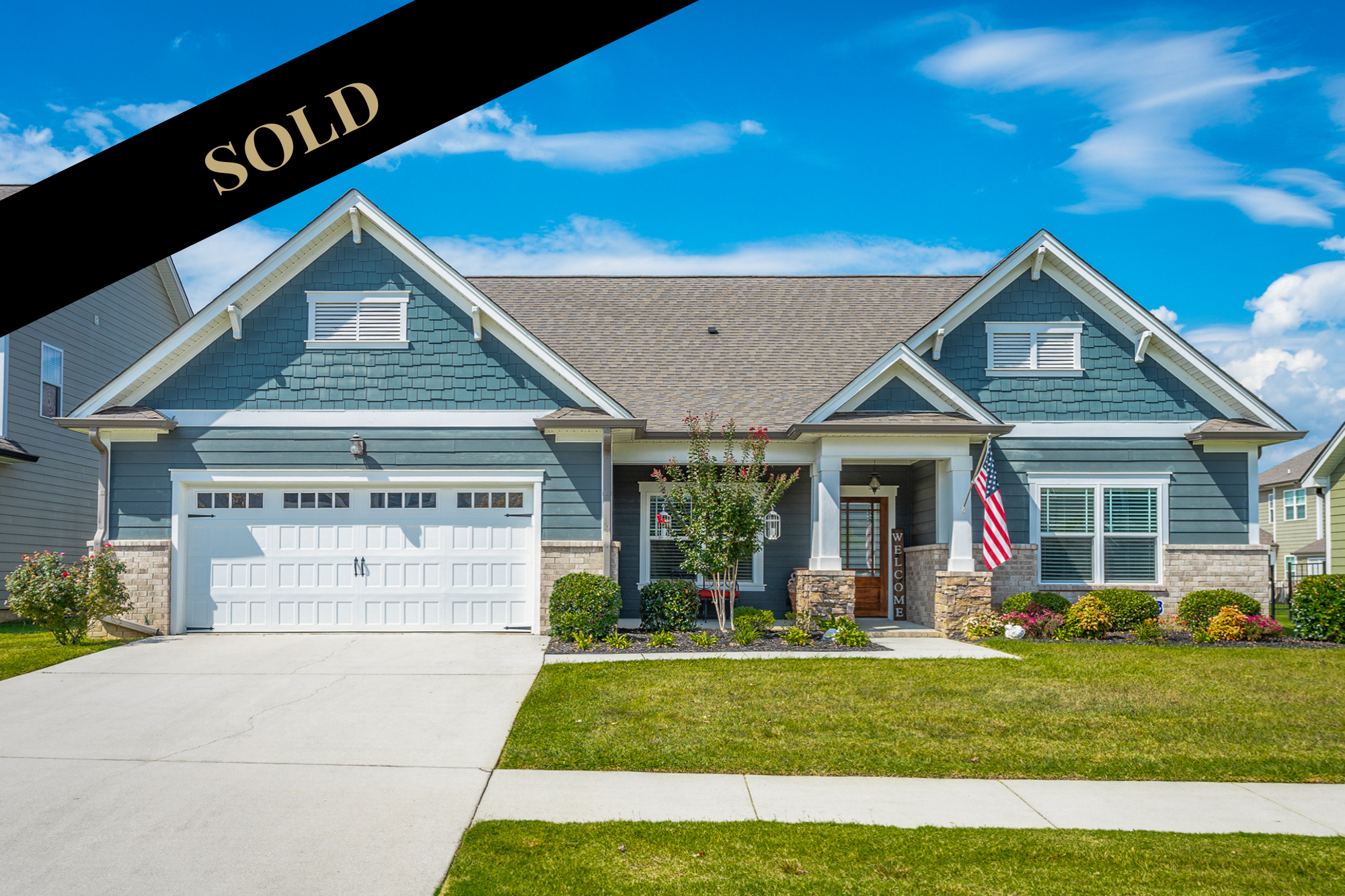 Front of 8462 River Birch Loop at blue craftsman home with front porch us flag and red door.   Home has Sold